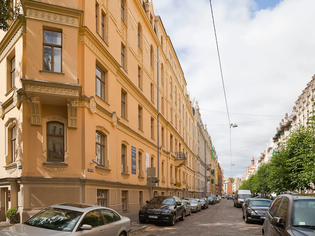 Alberto gatvė su geltonais Art Nouveau namais ir grįstu keliu, kuriame stovi automobiliai