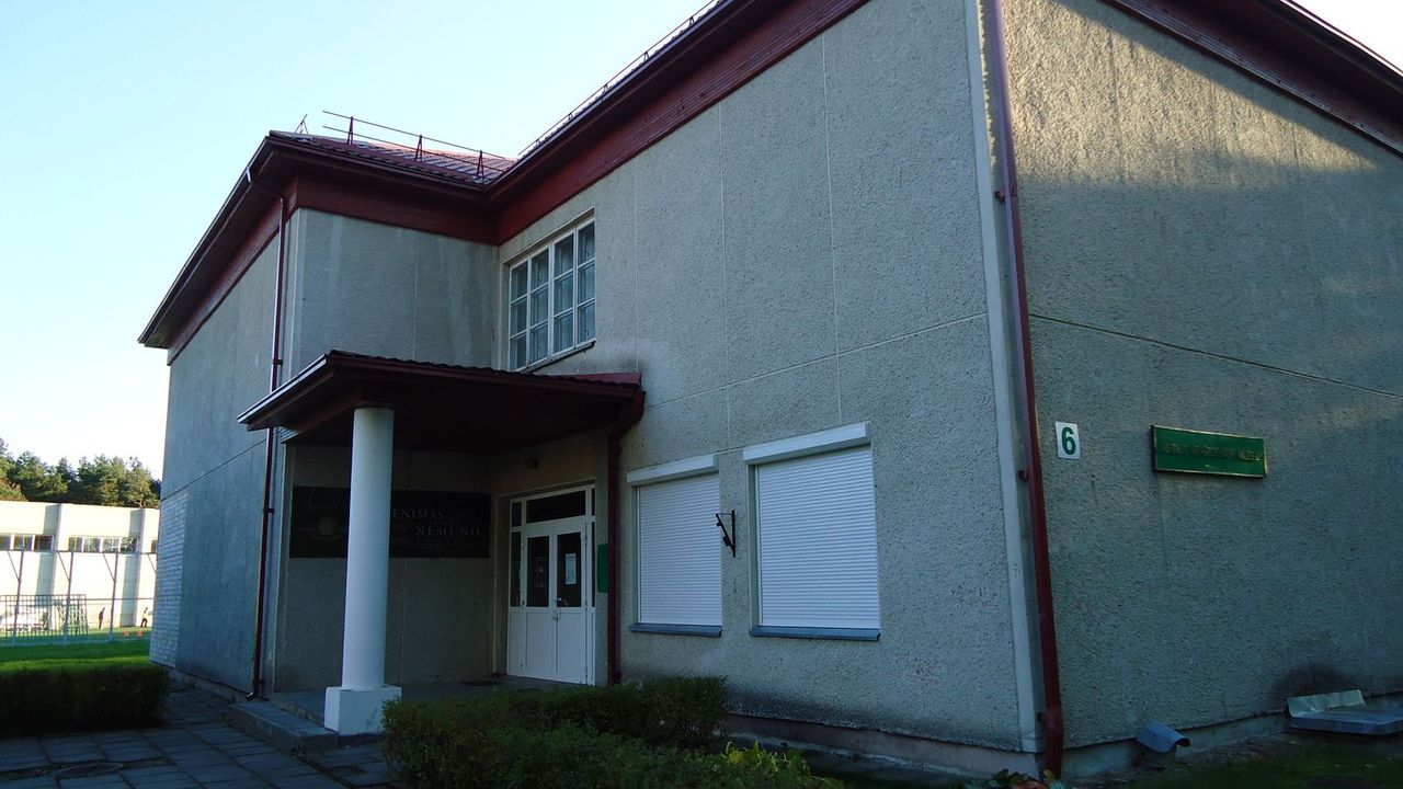 Šviesus Alytaus kraštotyros muziejaus pastatas su raudonu stogo kraštu ir gėlių lysve priekyje