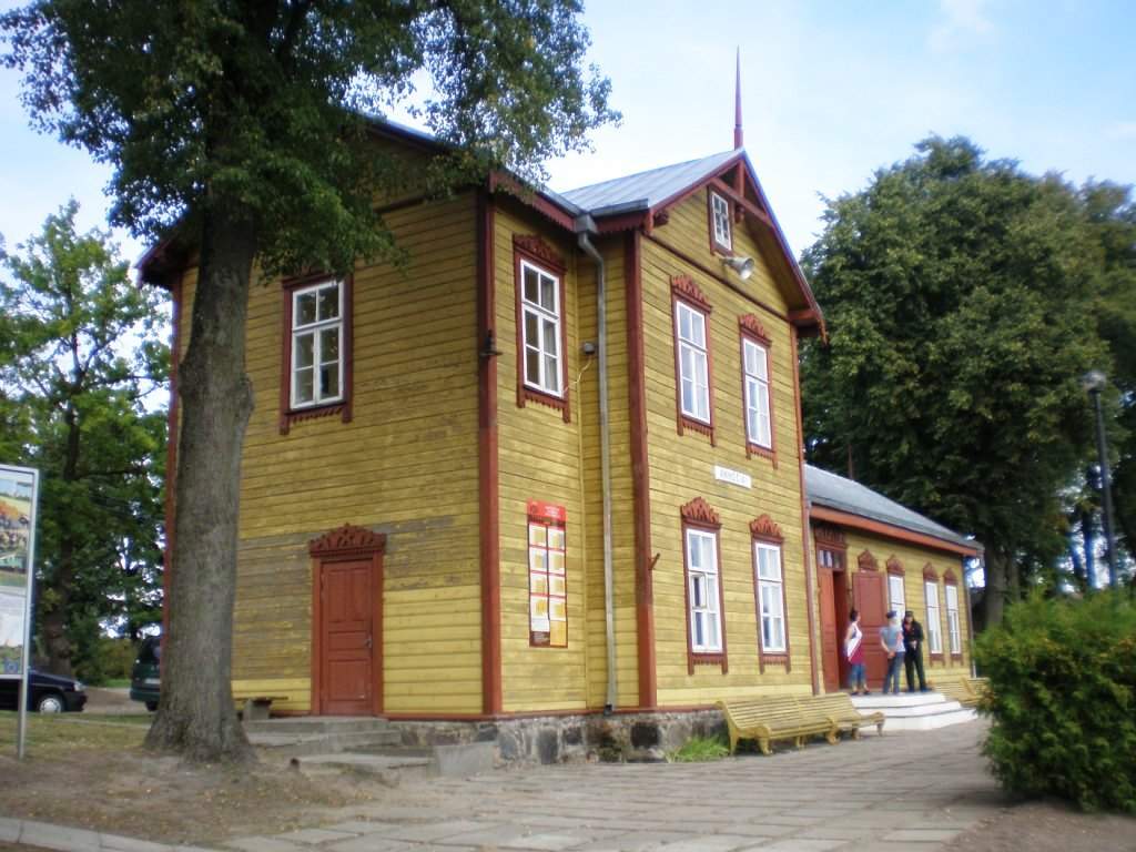 Geltona dviaukštė medinė Anykščių siaurojo geležinkelio stotis su raudonais langų rėmais ir suoleliais
