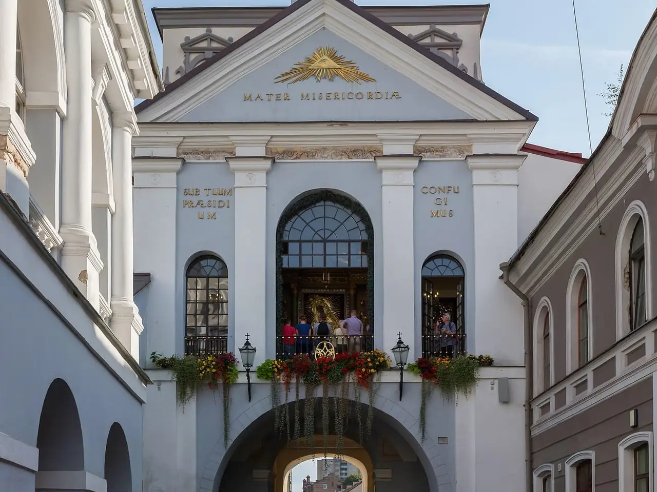 Balti Aušros Vartai su koplyčios langu virš arkos ir gėlėmis ant balkono