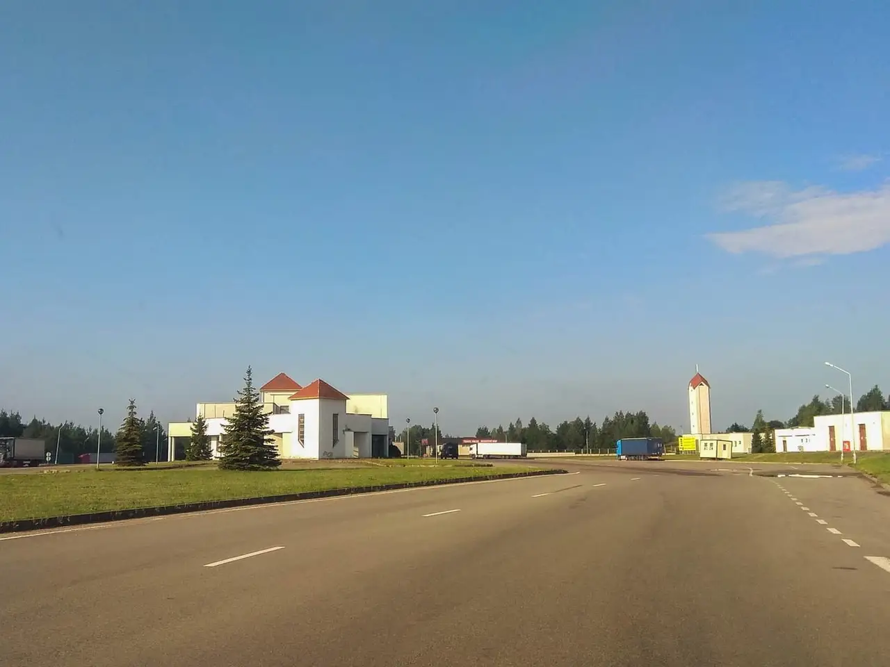 Tuščias kelias ir baltos Budziskos–Kalvarijos pasienio punkto patalpos giedrą dieną