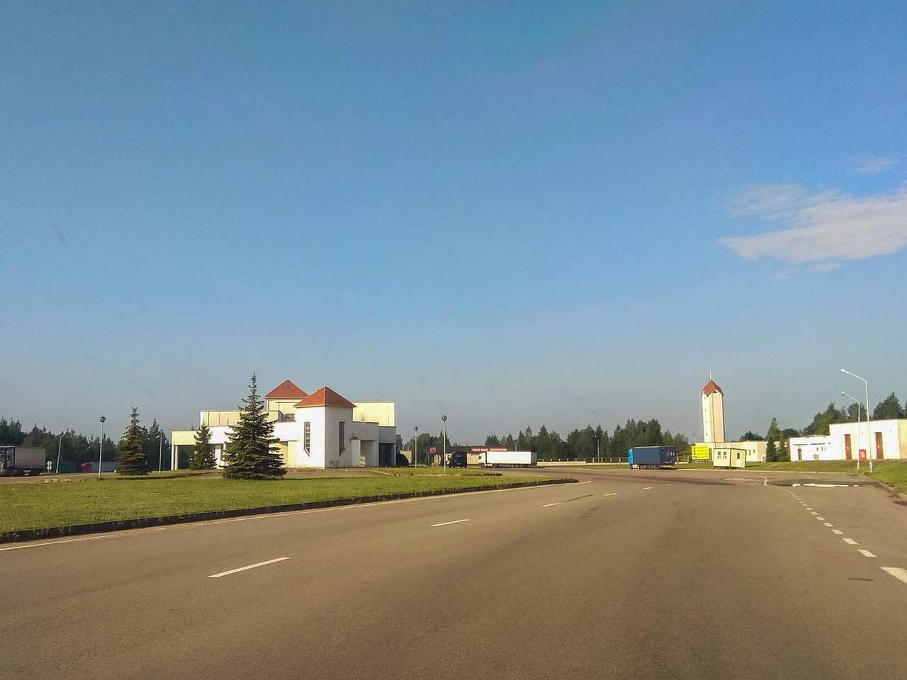 Tuščias kelias ir baltos Budziskos–Kalvarijos pasienio punkto patalpos giedrą dieną