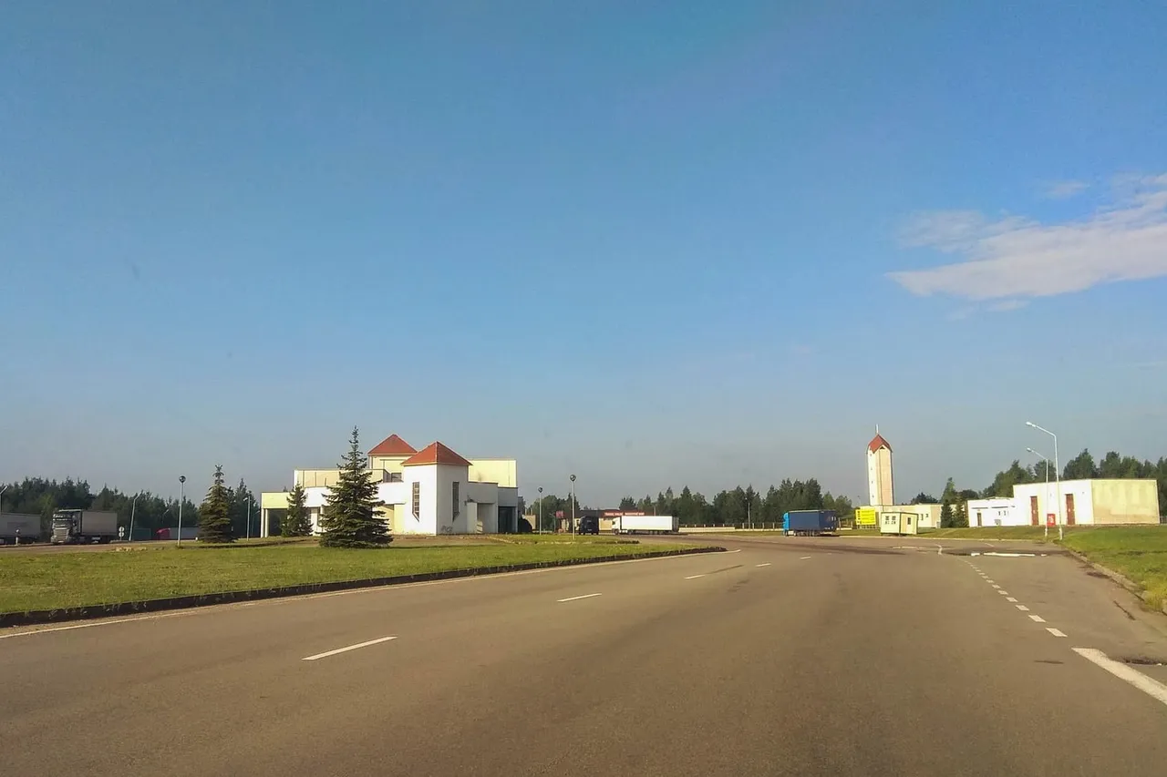 Tuščias kelias ir baltos Budziskos–Kalvarijos pasienio punkto patalpos giedrą dieną