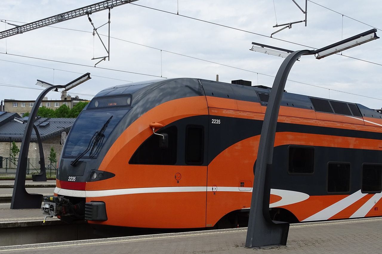 Oranžinis „Elron“ elektrinis traukinys perone Taline po kontaktiniais laidais