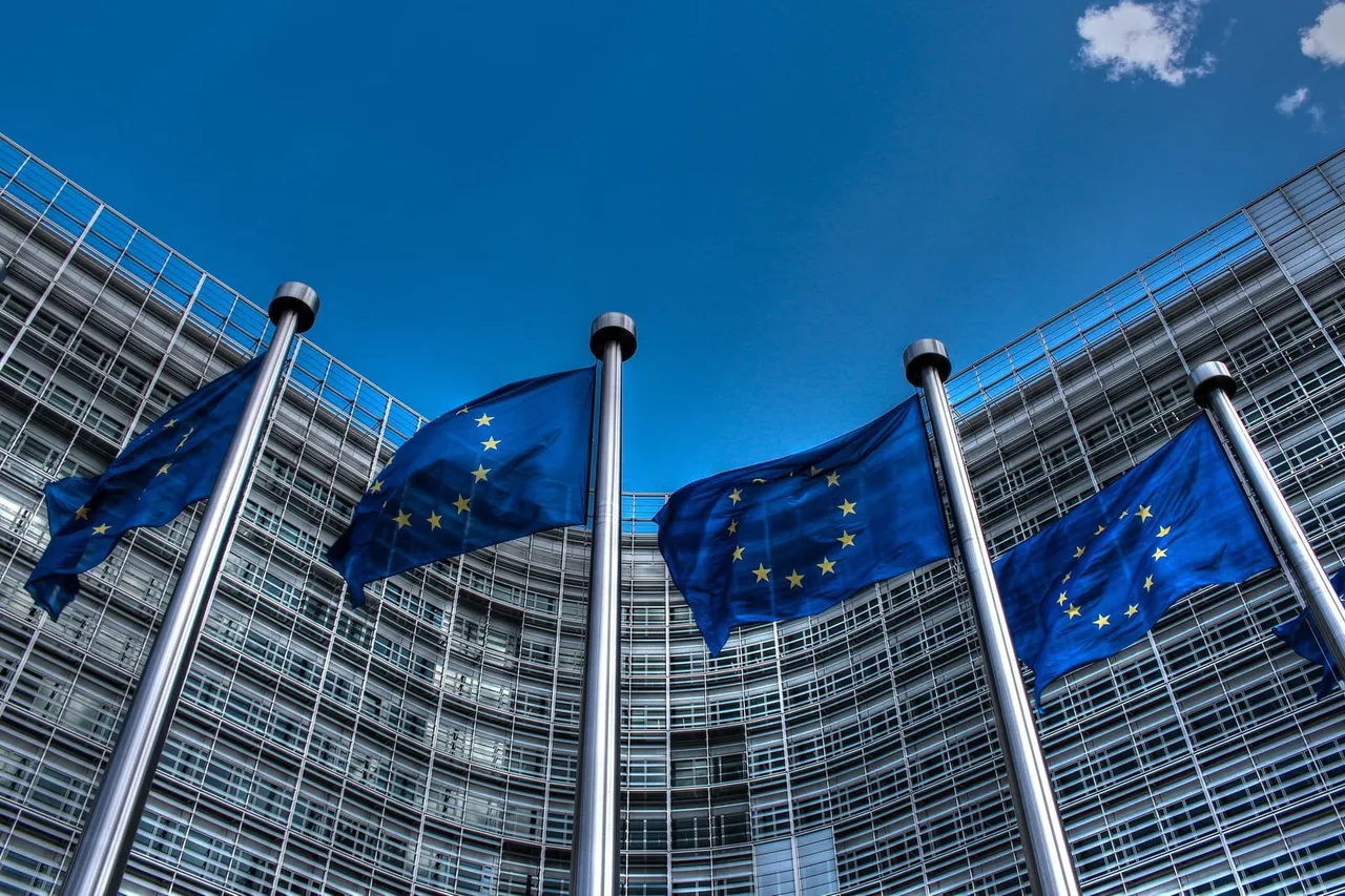 Mėlynos Europos Sąjungos vėliavos plazda prieš stiklinį pastato fasadą