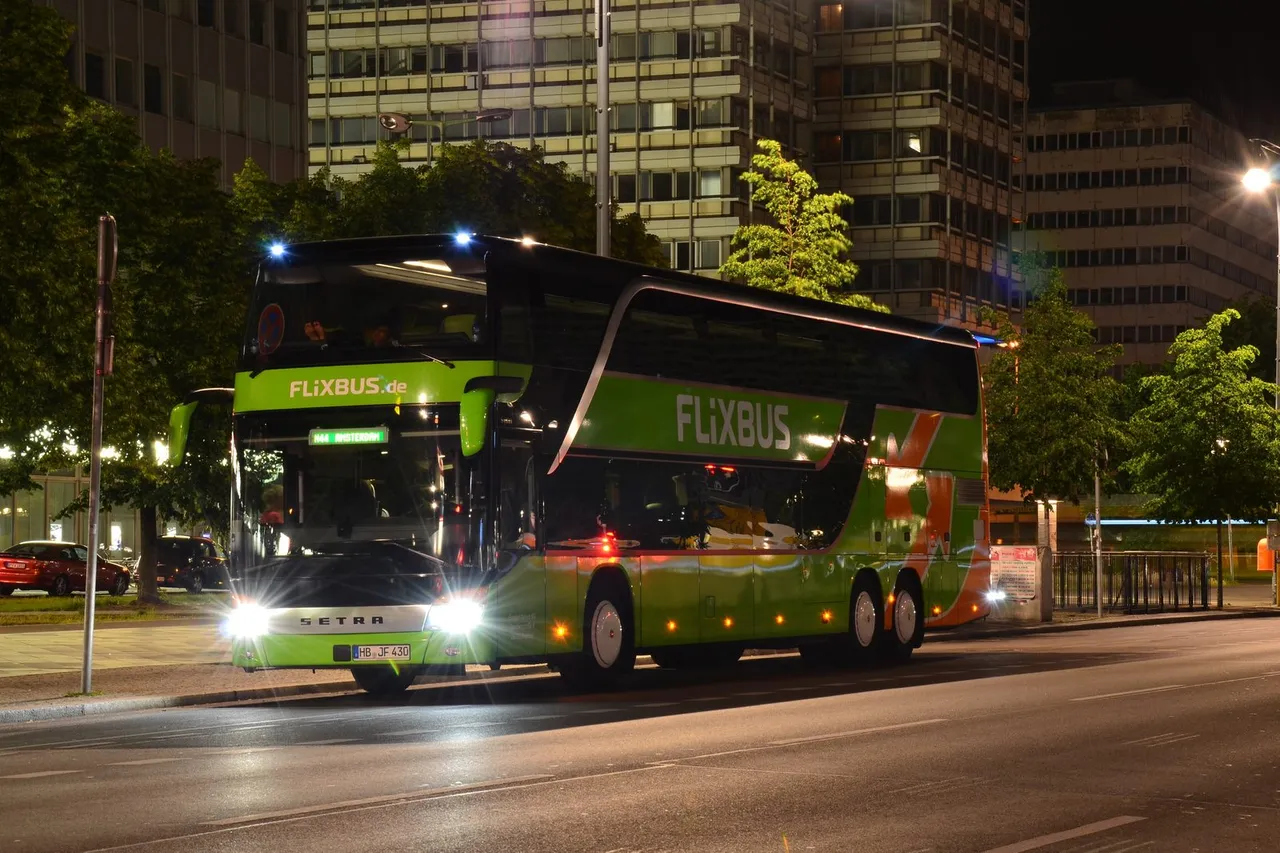 Žalias dviaukštis „FlixBus“ autobusas vakare stovi gatvėje šalia aukštų pastatų