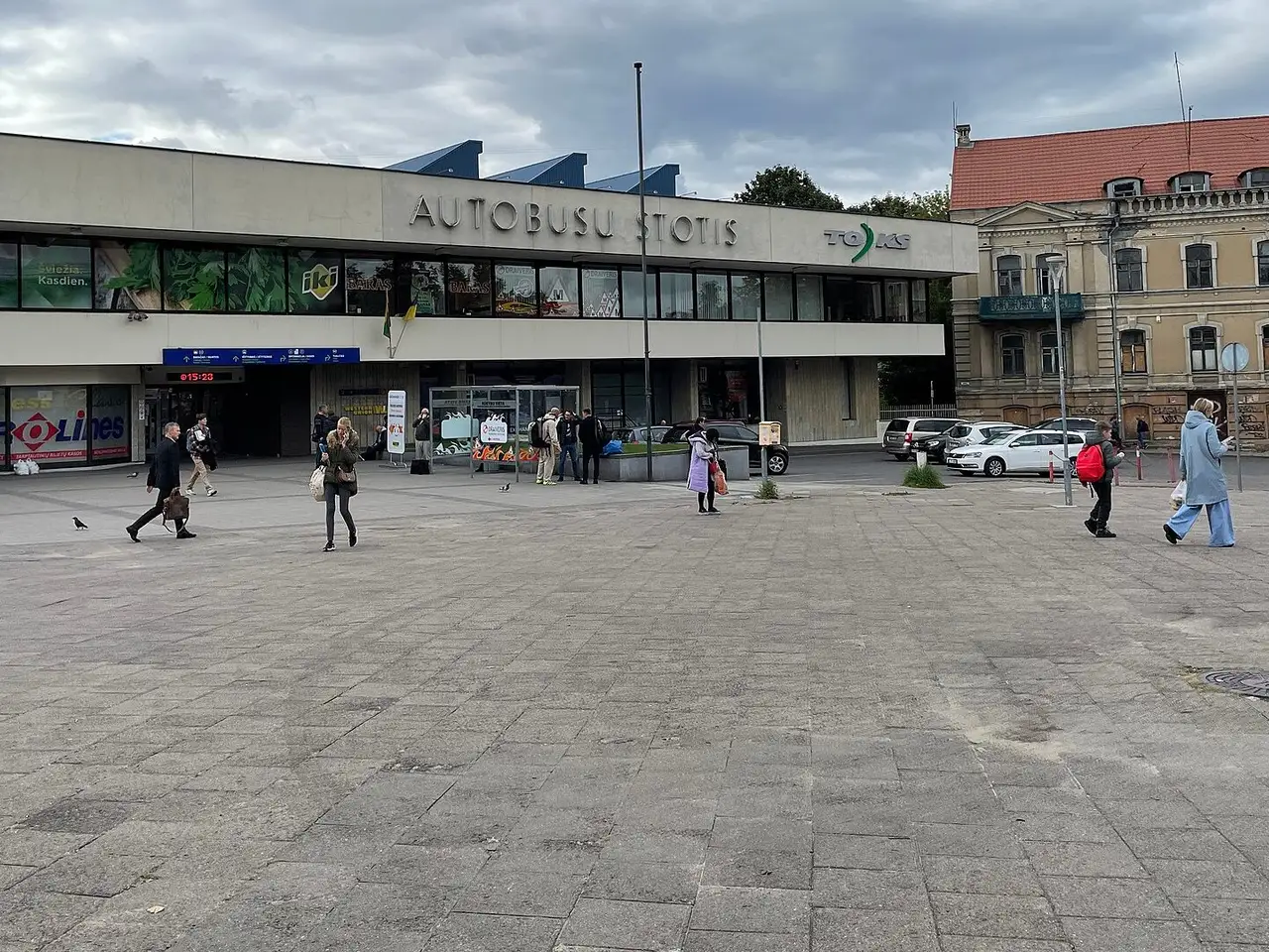 Vilniaus autobusų stoties pastatas debesuotą dieną, priešais aikštėje eina keleiviai