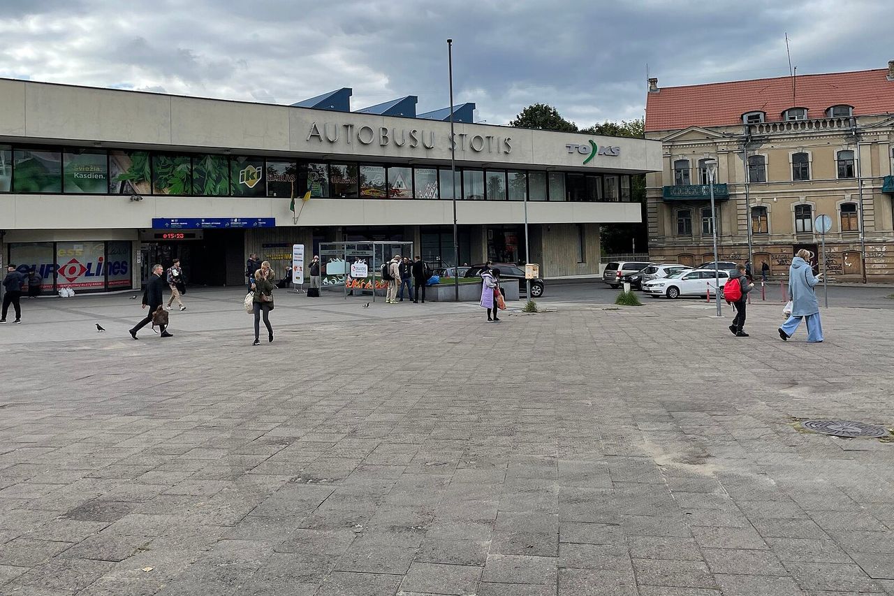Vilniaus autobusų stoties pastatas debesuotą dieną, priešais aikštėje eina keleiviai
