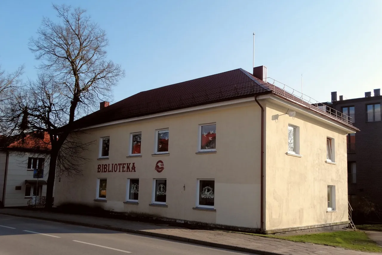 Geltonas dviejų aukštų Gargždų bibliotekos pastatas su raudonu stogu ir plikais medžiais