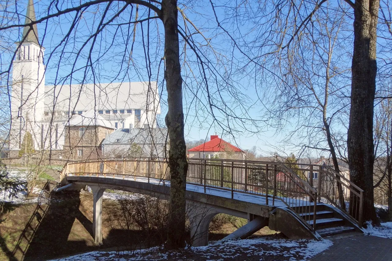 Mediniai pėsčiųjų viaduko turėklai Gargžduose, fone matosi balta bažnyčia ir pliki medžiai