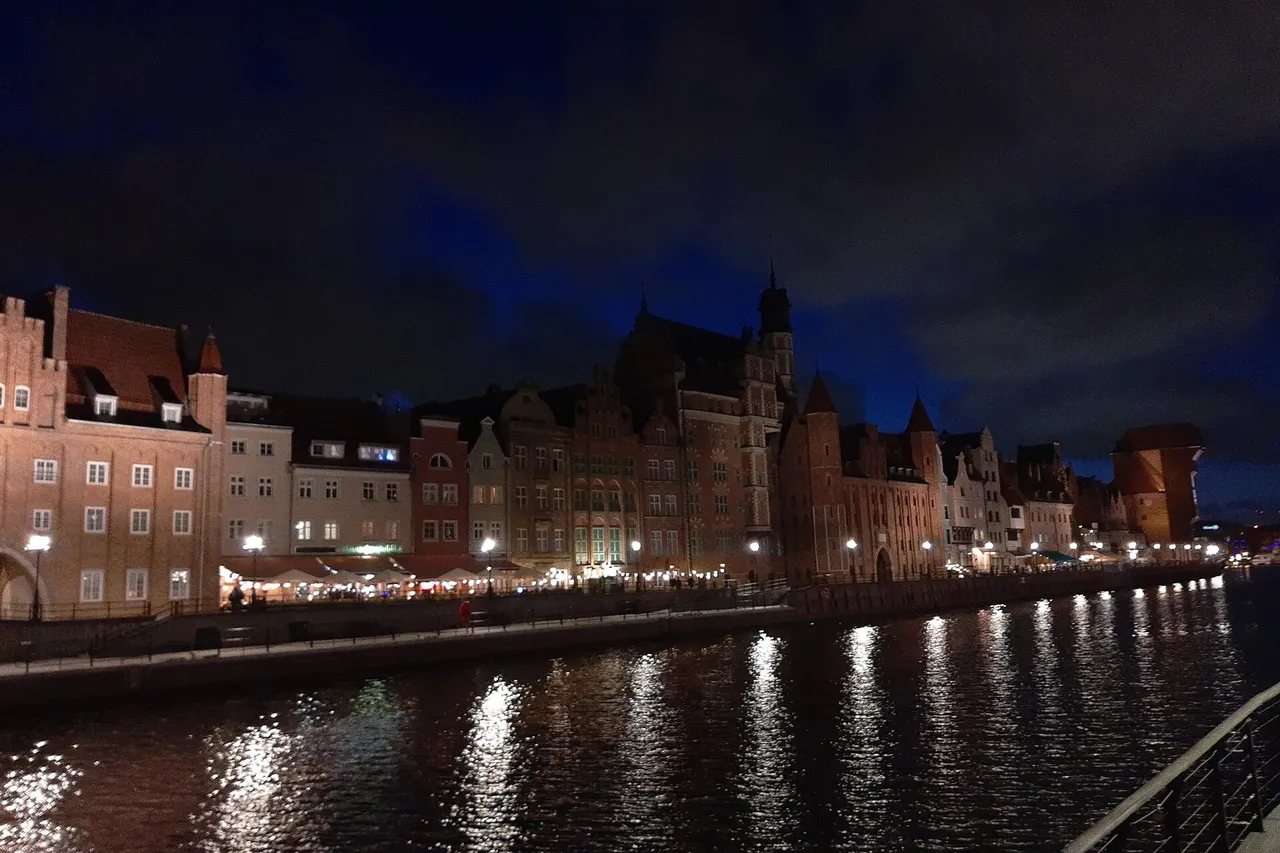 Vakarinis Motławos krantas Gdanske su apšviestais senamiesčio namais ir uosto krano siluetu