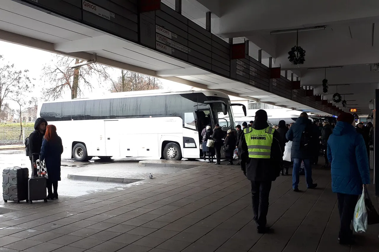 Baltas tolimojo susisiekimo autobusas Vilniaus autobusų stotyje, prie durų renkasi keleiviai su lagaminais