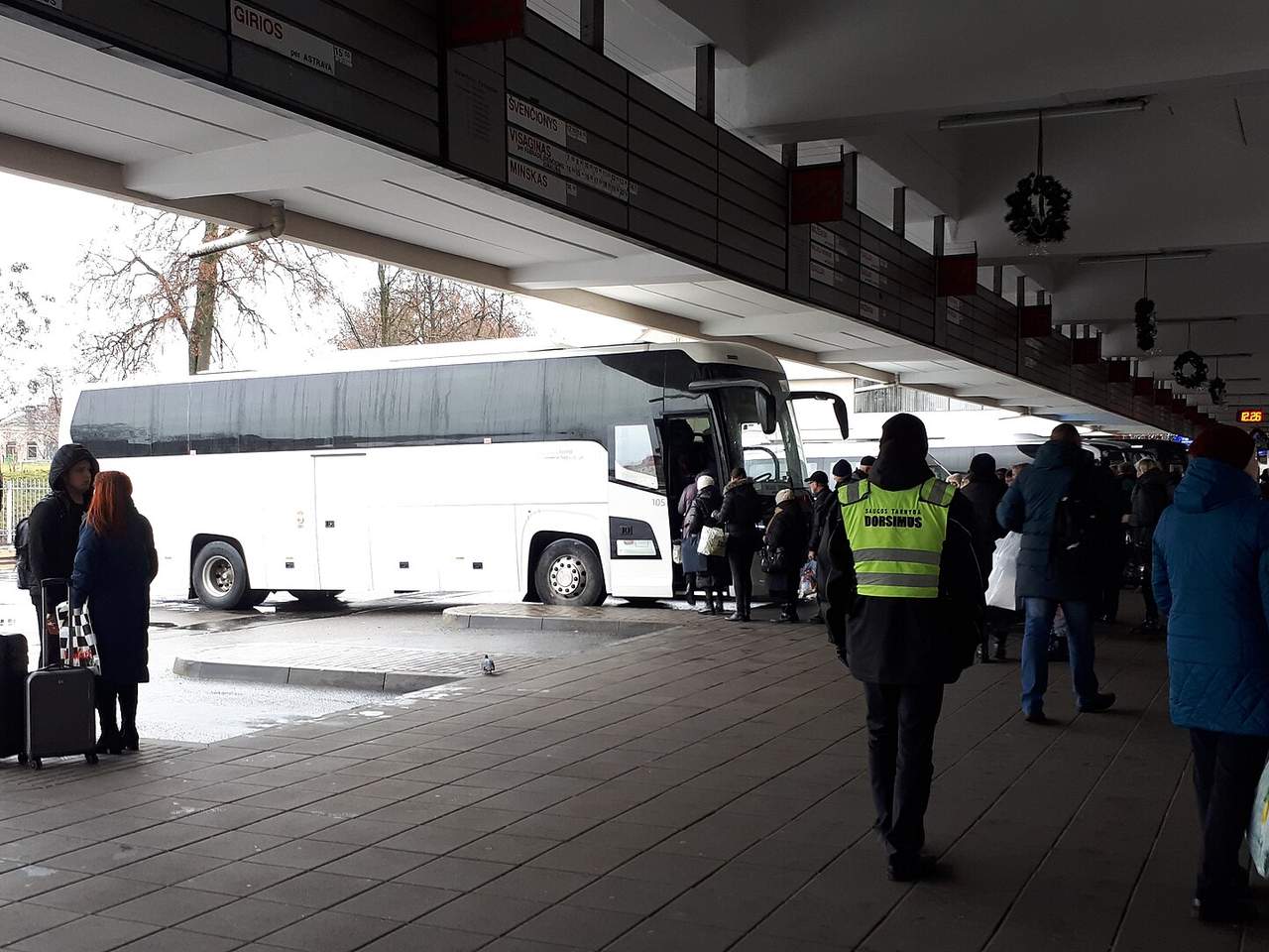 Baltas tolimojo susisiekimo autobusas Vilniaus autobusų stotyje, prie durų renkasi keleiviai su lagaminais