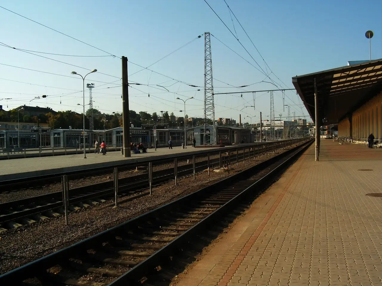 Peronas ir bėgiai Vilniaus geležinkelio stotyje giedrą rytą, tolumoje keli keleiviai