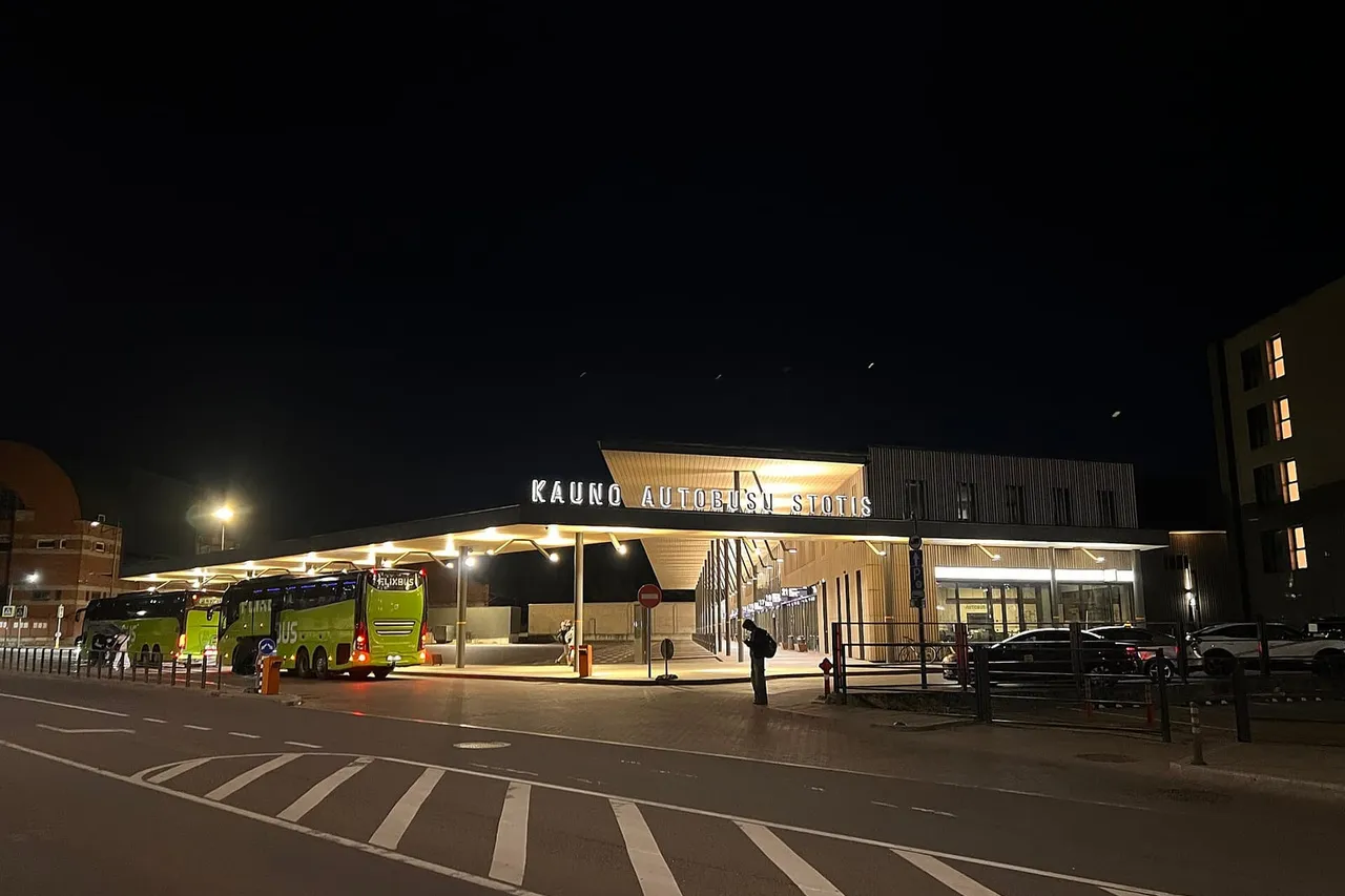 Naktį apšviesta Kauno autobusų stotis su užrašu ir žaliais autobusais po stogine