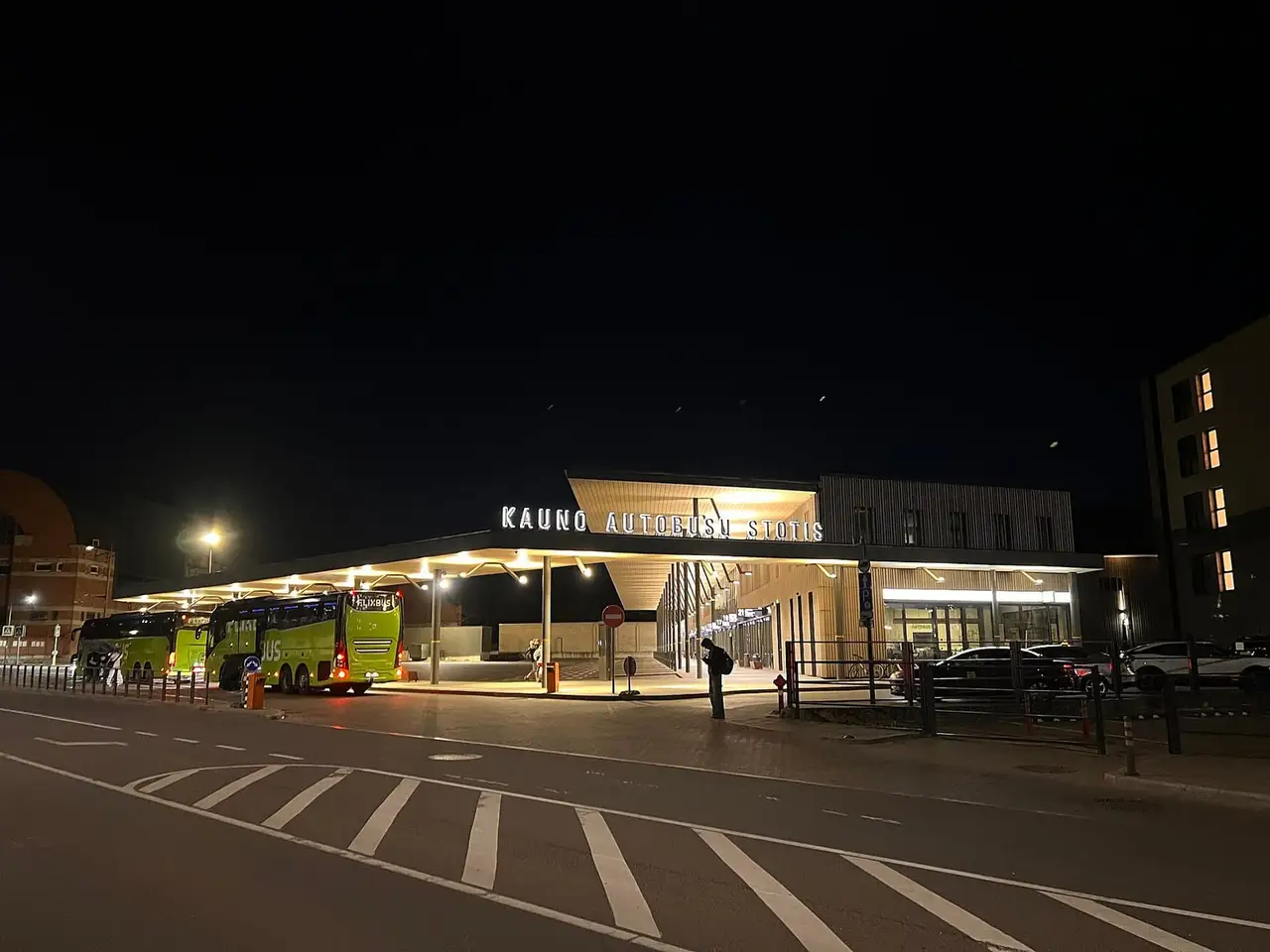 Naktį apšviesta Kauno autobusų stotis su užrašu ir žaliais autobusais po stogine