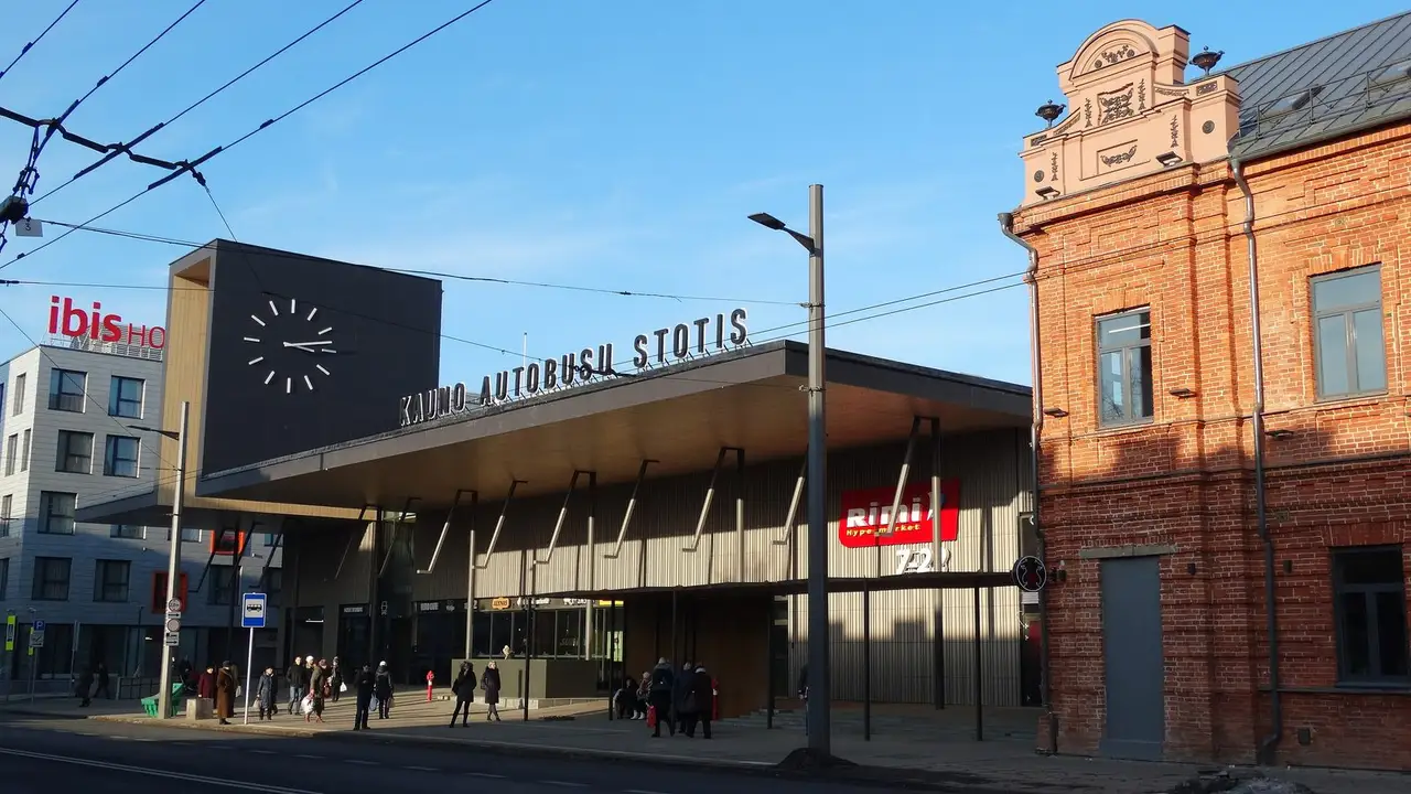 Naujas Kauno autobusų stoties pastatas su dideliu laikrodžiu, užrašu ir raudonų plytų pastatu šalia
