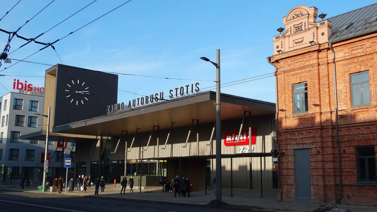 Naujas Kauno autobusų stoties pastatas su dideliu laikrodžiu, užrašu ir raudonų plytų pastatu šalia