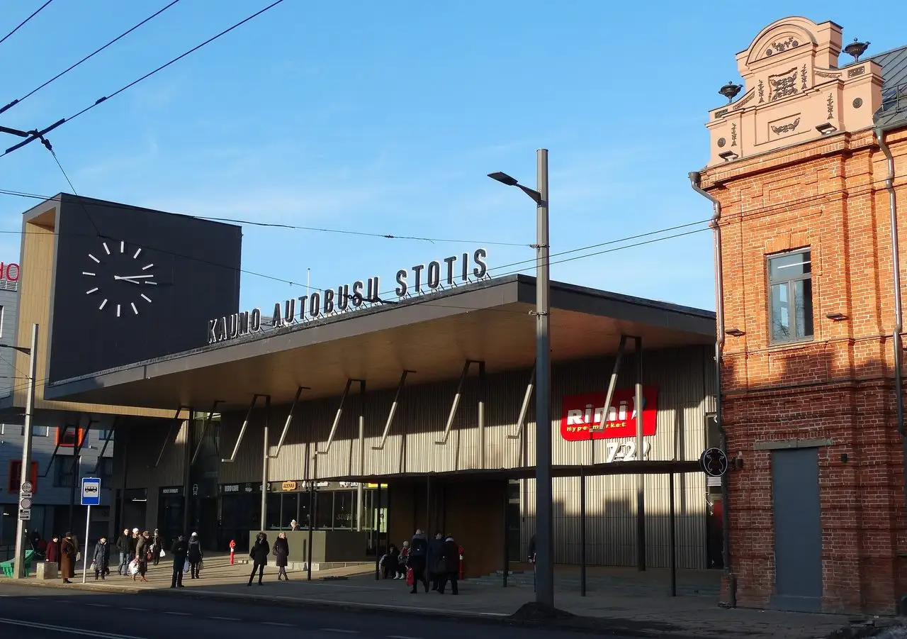 Naujas Kauno autobusų stoties pastatas su dideliu laikrodžiu, užrašu ir raudonų plytų pastatu šalia