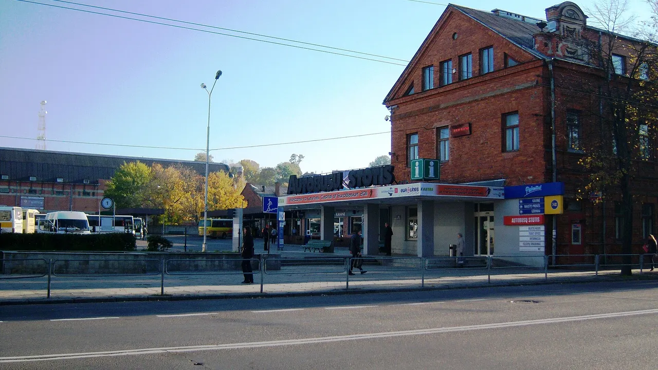 Raudonų plytų Kauno autobusų stoties pastatas su užrašu „Autobusų stotis“ ir stovintys autobusai