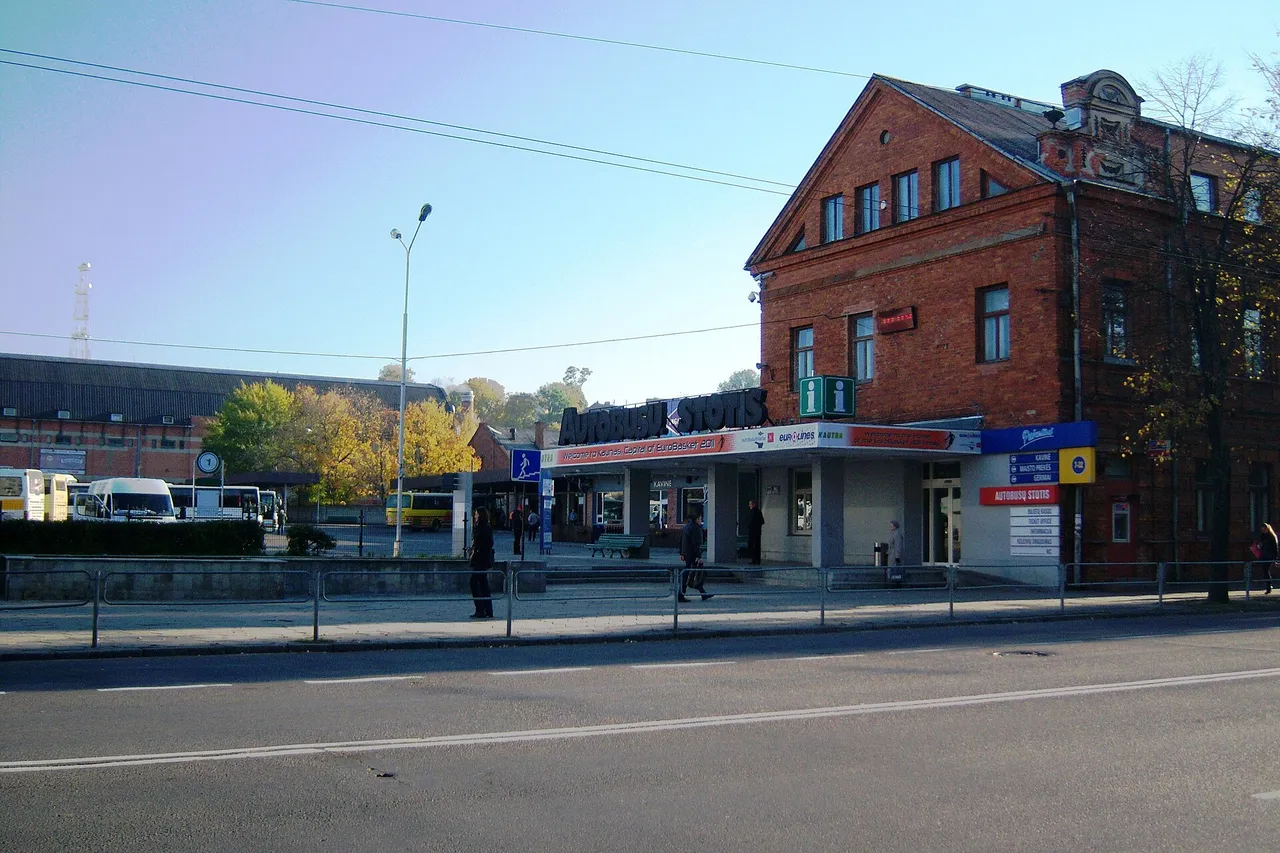 Raudonų plytų Kauno autobusų stoties pastatas su užrašu „Autobusų stotis“ ir stovintys autobusai