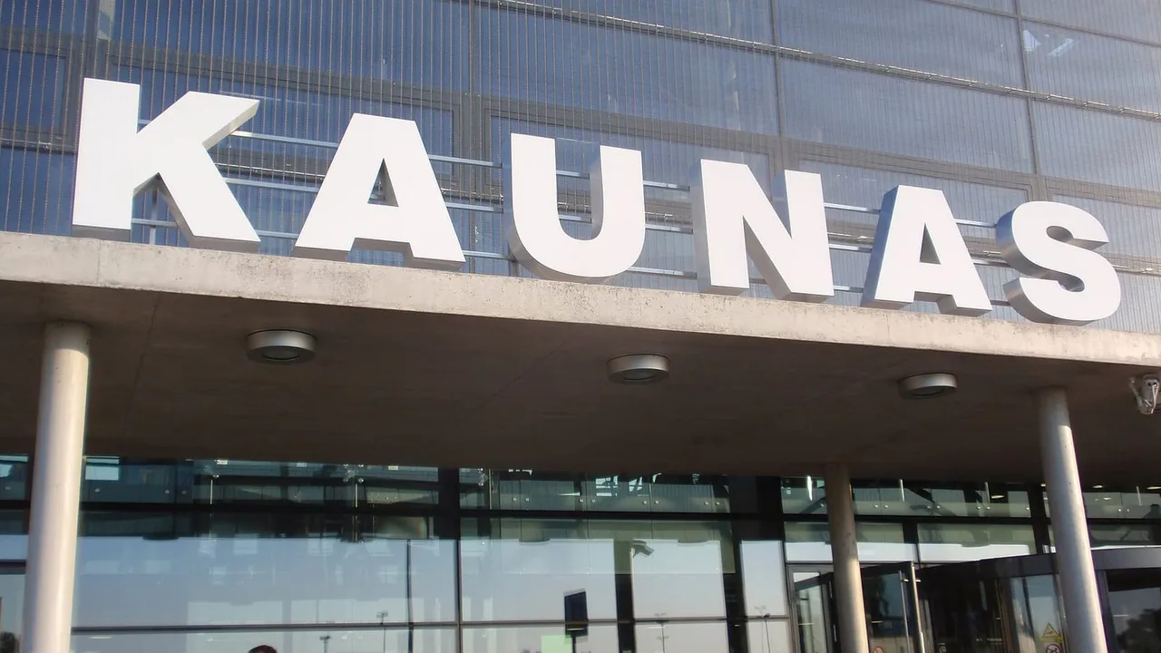 Baltos raidės „Kaunas“ ant oro uosto terminalo stogelio, po juo stikliniai įėjimo langai ir žmonės