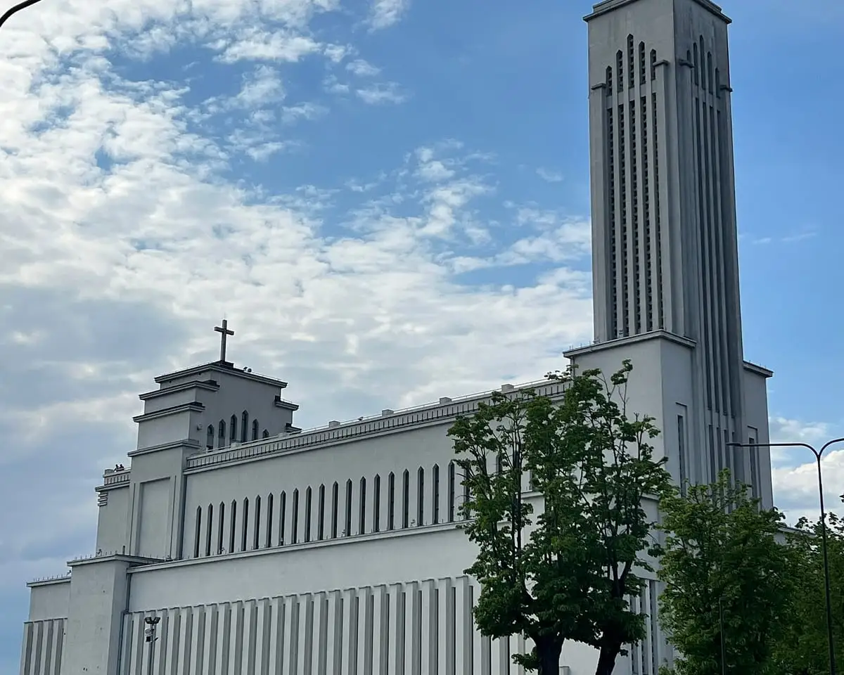 Šviesi Kristaus Prisikėlimo bazilika su aukštu stačiakampiu bokštu ir medžiu priekyje