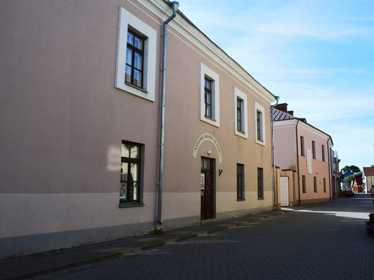 Dviejų aukštų gelsvas Kėdainių krašto muziejaus pastatas su langais ir tuščia gatve