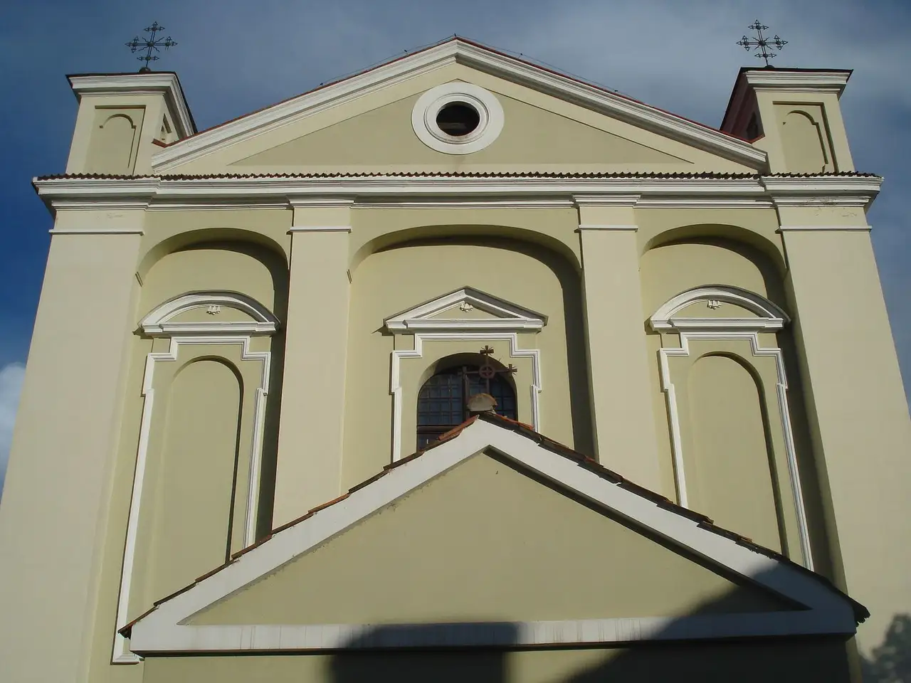 Gelsvas Kėdainių evangelikų reformatų bažnyčios fasadas su baltais apdailos akcentais ir kryžiais