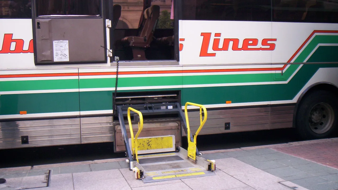 Tolimojo susisiekimo autobuso šone nuleista geltonais turėklais aprūpinta keltuvo platforma vežimėliui