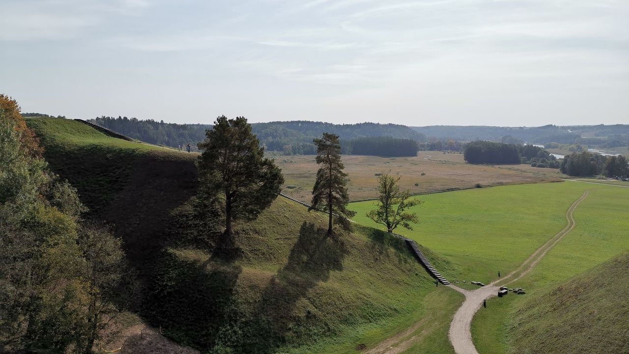 Žoliniai Kernavės piliakalniai su laiptais ir plati Neries slėnio panorama po šviesiu dangumi