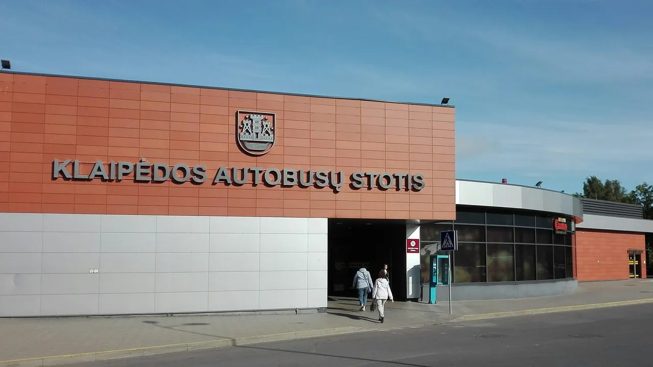 Klaipėdos autobusų stoties pastatas su miesto herbu ir užrašu virš įėjimo, priekyje praeina du keleiviai