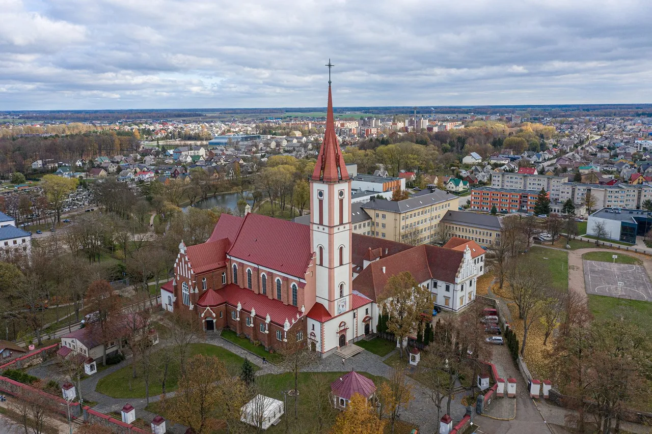 Raudonų stogų Kretingos Bernardinų vienuolyno bažnyčia su bokštu, aplink miesto namai ir žaluma