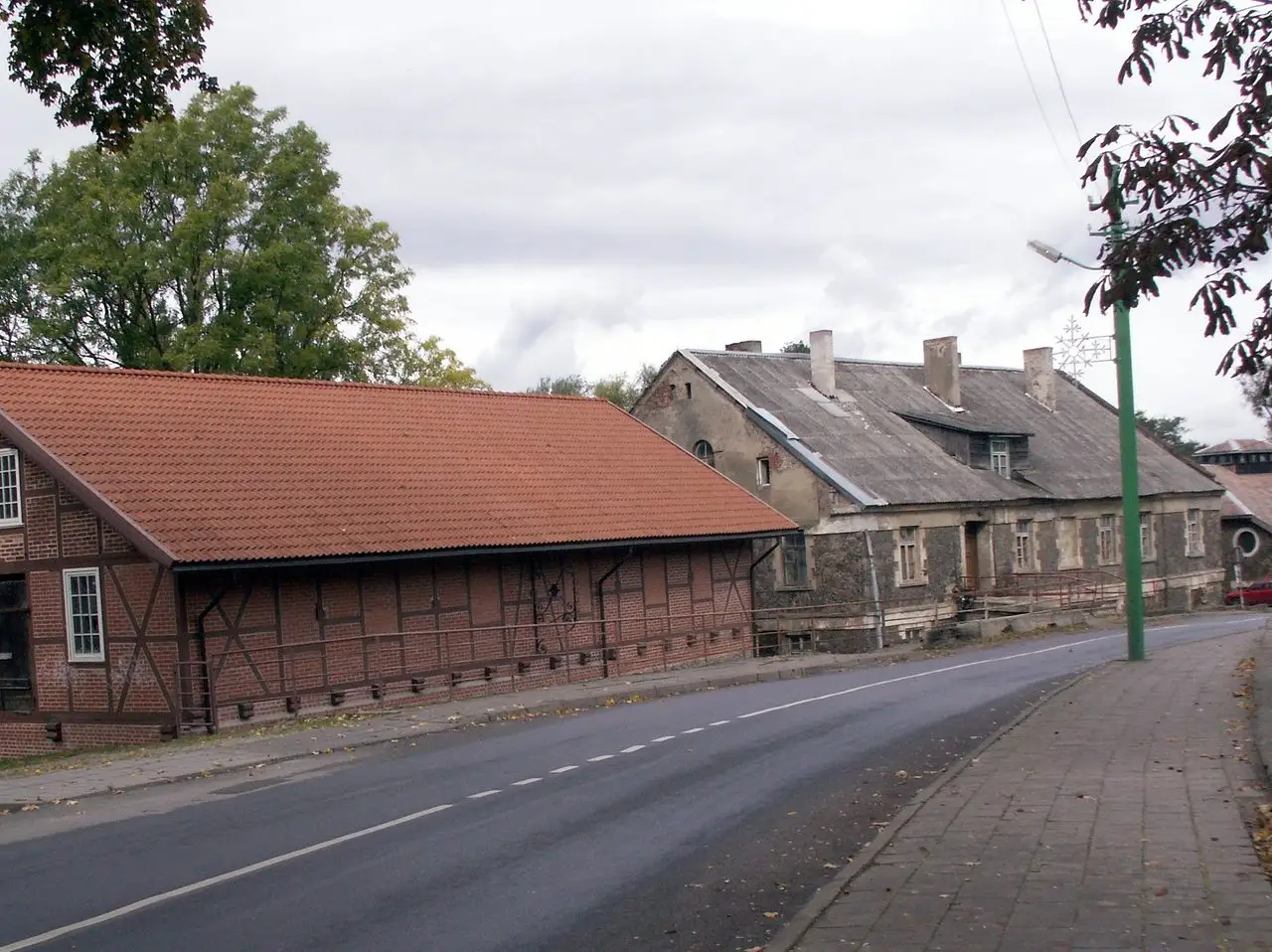 Raudonų čerpių stogu dengtas fachverkinis Kretingos vandens malūno pastatas prie kelio, už jo seni namai