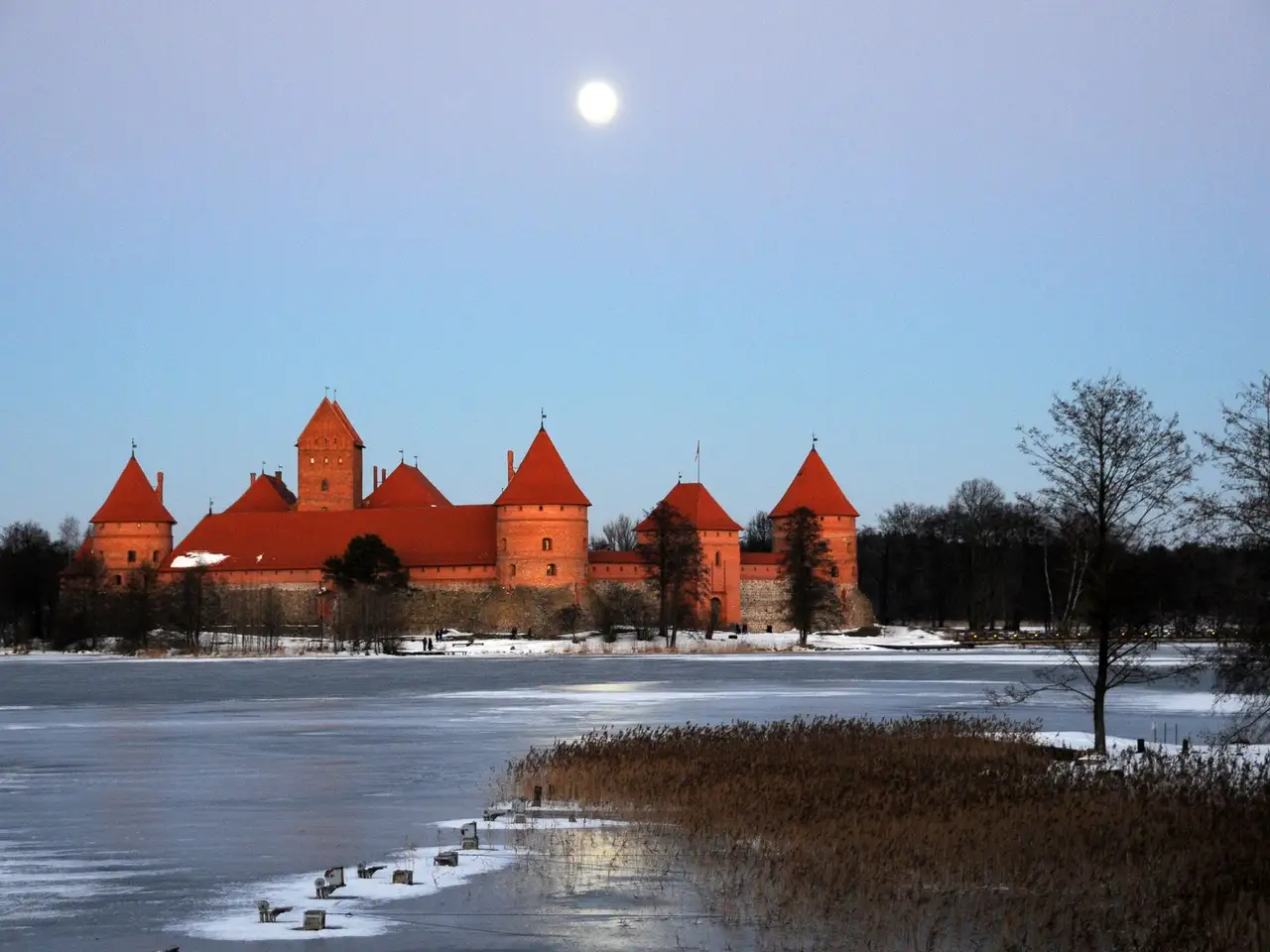 Raudonų plytų Trakų Salos pilis prie užšalusio ežero, virš jos šviečia mėnulis