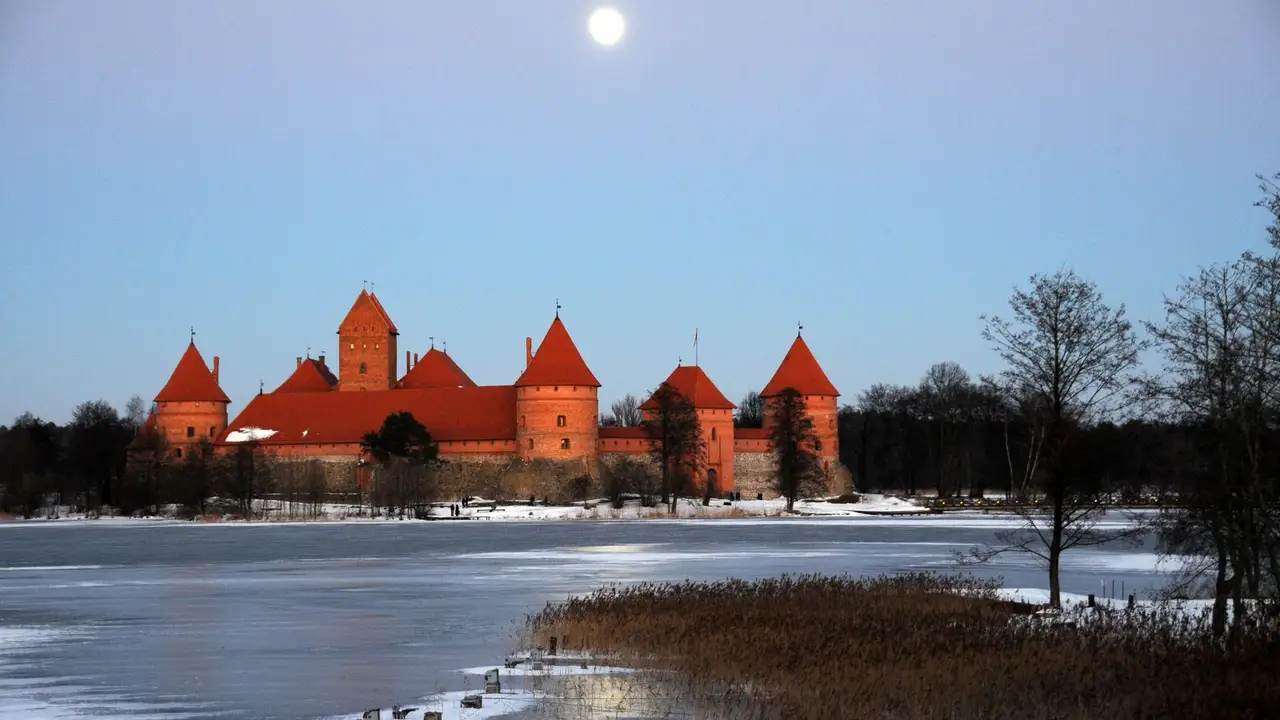 Raudonų plytų Trakų Salos pilis prie užšalusio ežero, virš jos šviečia mėnulis
