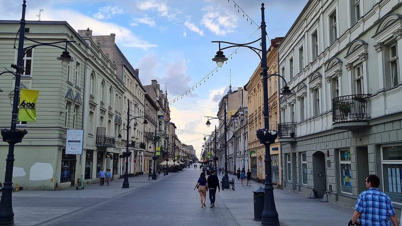 Piotrkowskos gatvė Lodzėje: pėstieji tarp istorinių pastatų su žibintais ir dangumi su debesimis
