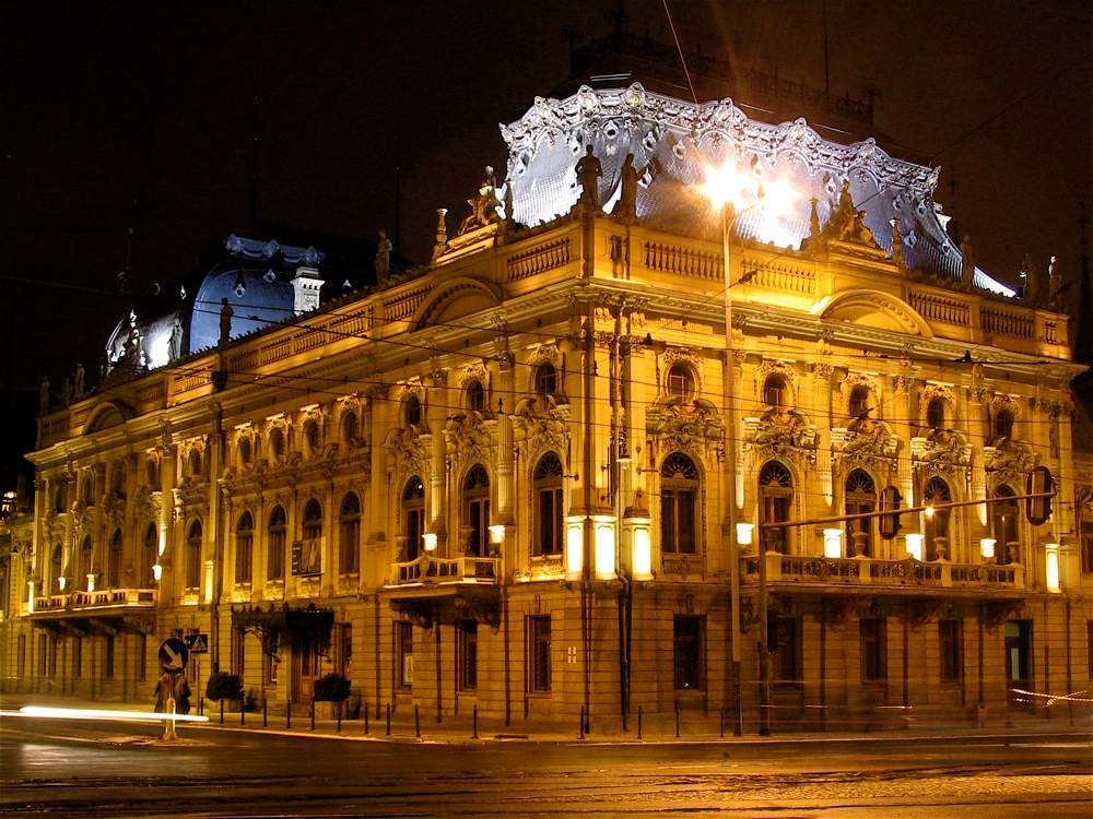 Naktį apšviestas Poznańskių rūmų fasadas Lodzėje su mėlynais stogais ir žibintu priekyje