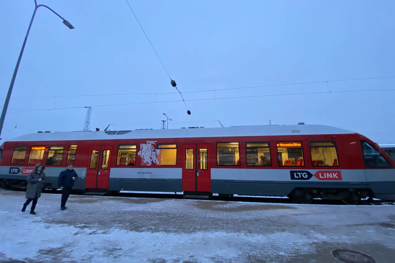 Raudonas „LTG Link“ traukinys žiemą perone, priekyje vaikšto keleiviai
