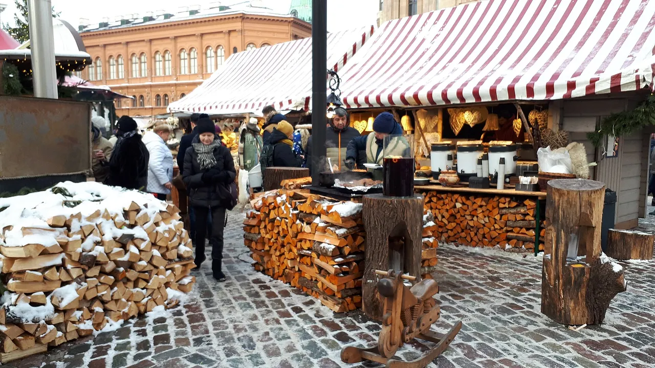 Šilto vyno kioskas Rygos Kalėdų turguje, sniegas ant grindinio ir sukrautos malkos