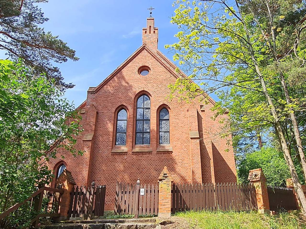 Raudonų plytų Nidos evangelikų liuteronų bažnyčia su smailiais langais tarp medžių
