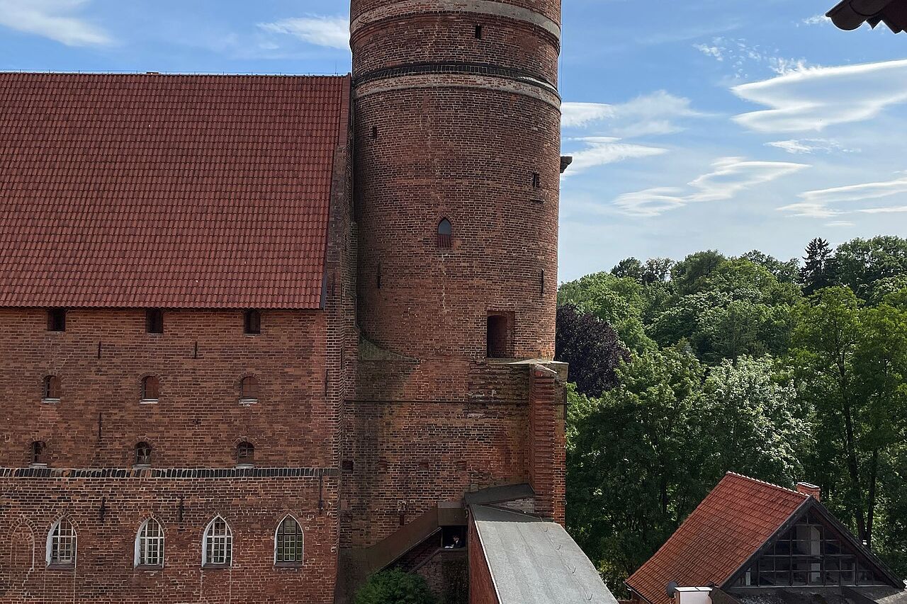 Olštyno pilies raudonų plytų bokštas su kūgio formos stogu ir pilies kiemas apačioje