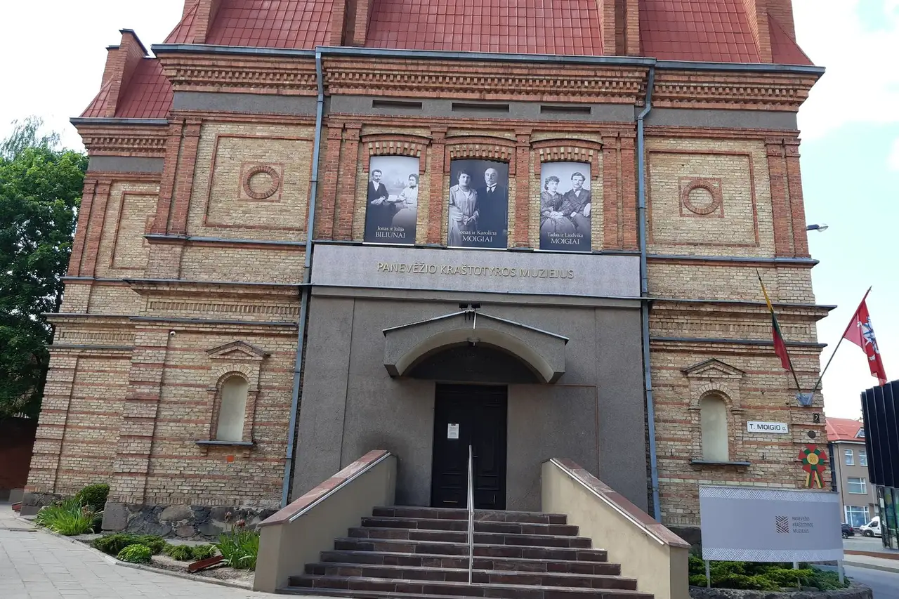 Raudonų plytų Panevėžio kraštotyros muziejaus fasadas su laiptais ir trimis nuotraukomis ant sienos