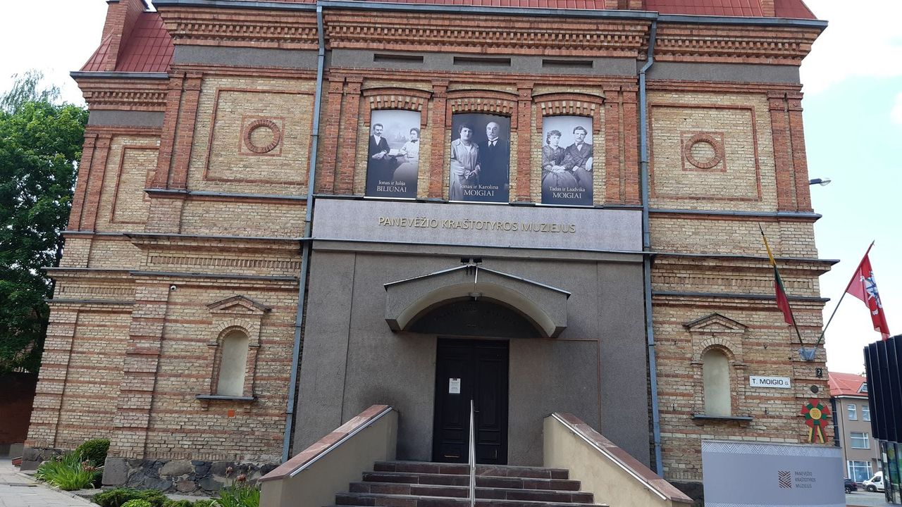 Raudonų plytų Panevėžio kraštotyros muziejaus fasadas su laiptais ir trimis nuotraukomis ant sienos