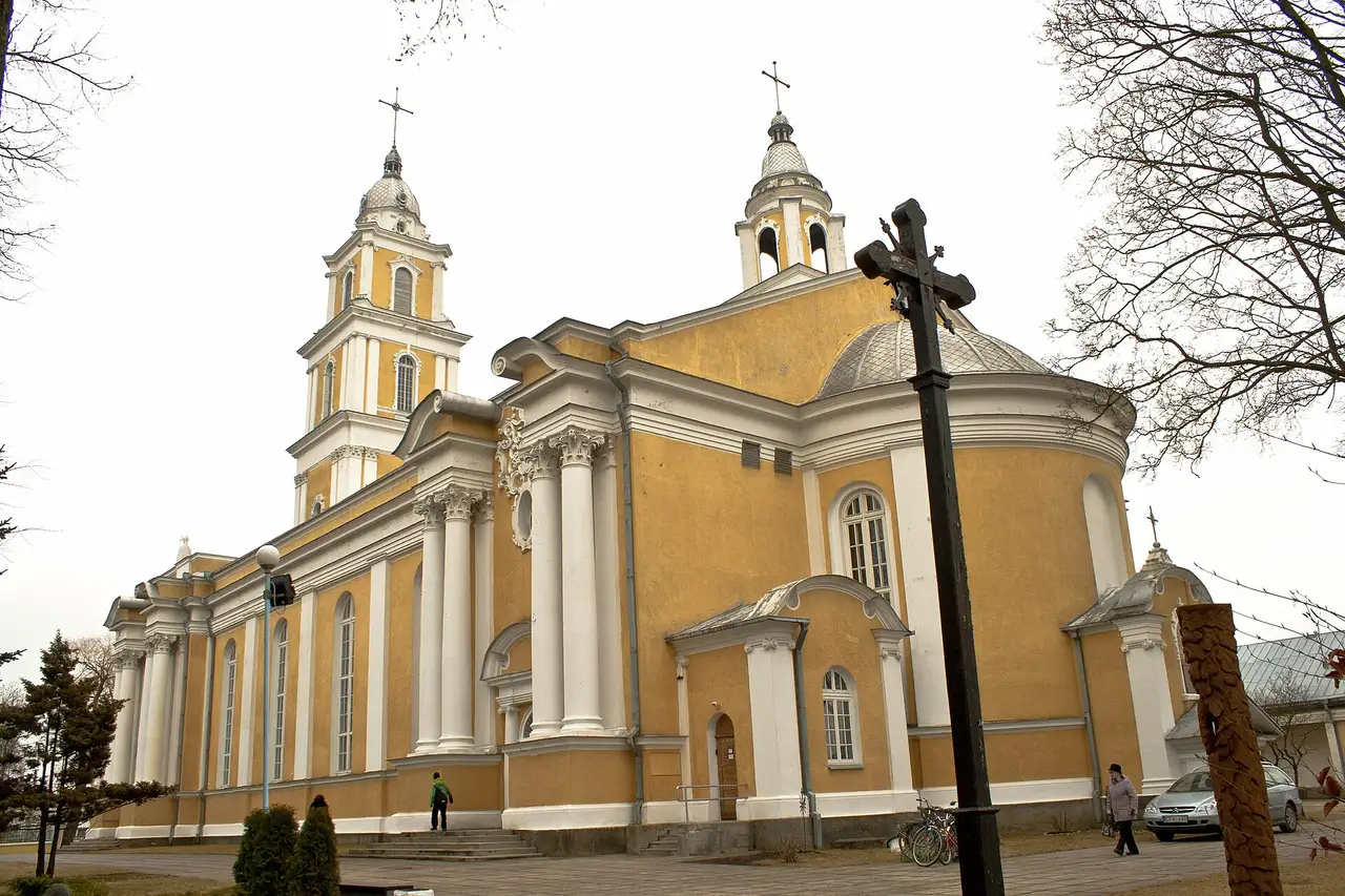 Geltona Panevėžio Kristaus Karaliaus katedra su bokštais, priekyje – medinis kryžius