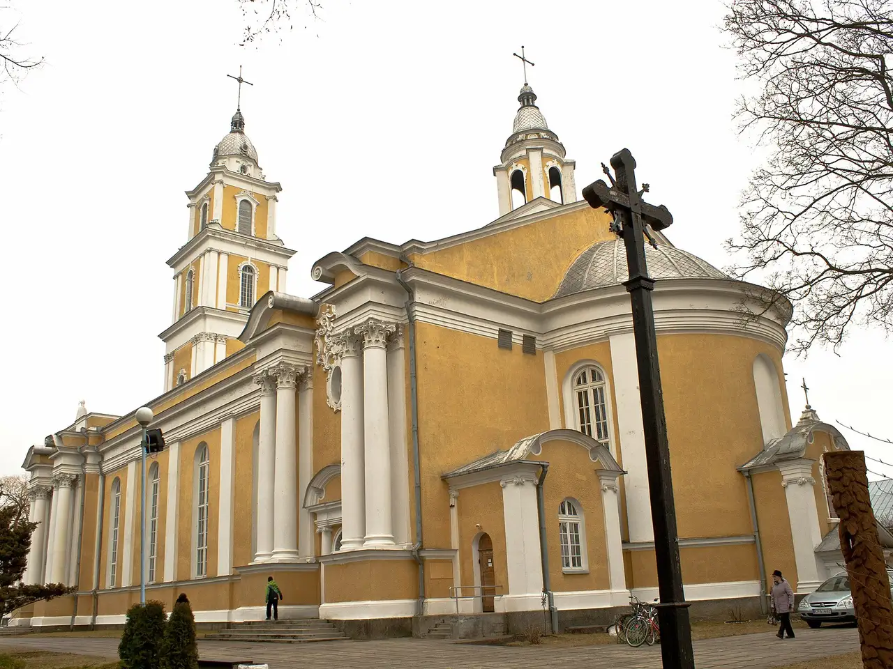 Geltona Panevėžio Kristaus Karaliaus katedra su bokštais, priekyje – medinis kryžius