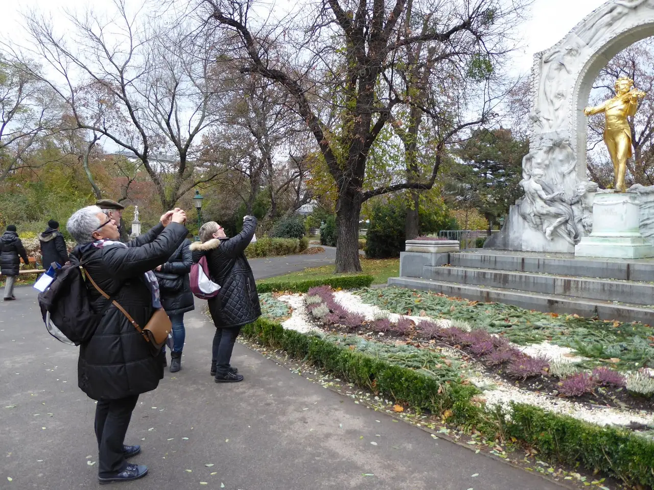 Turistai rudeniniame Vienos parke fotografuoja telefonais auksinį Johanno Strausso paminklą