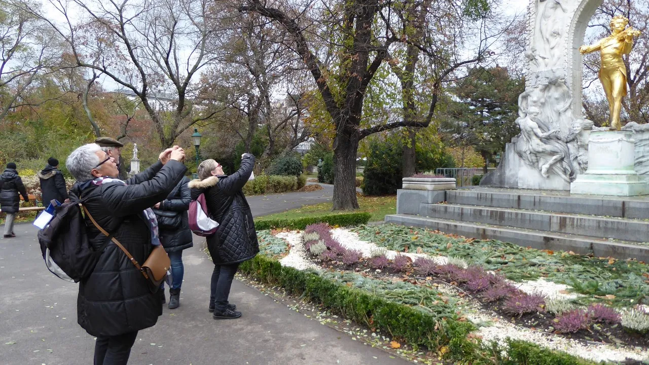 Turistai rudeniniame Vienos parke fotografuoja telefonais auksinį Johanno Strausso paminklą