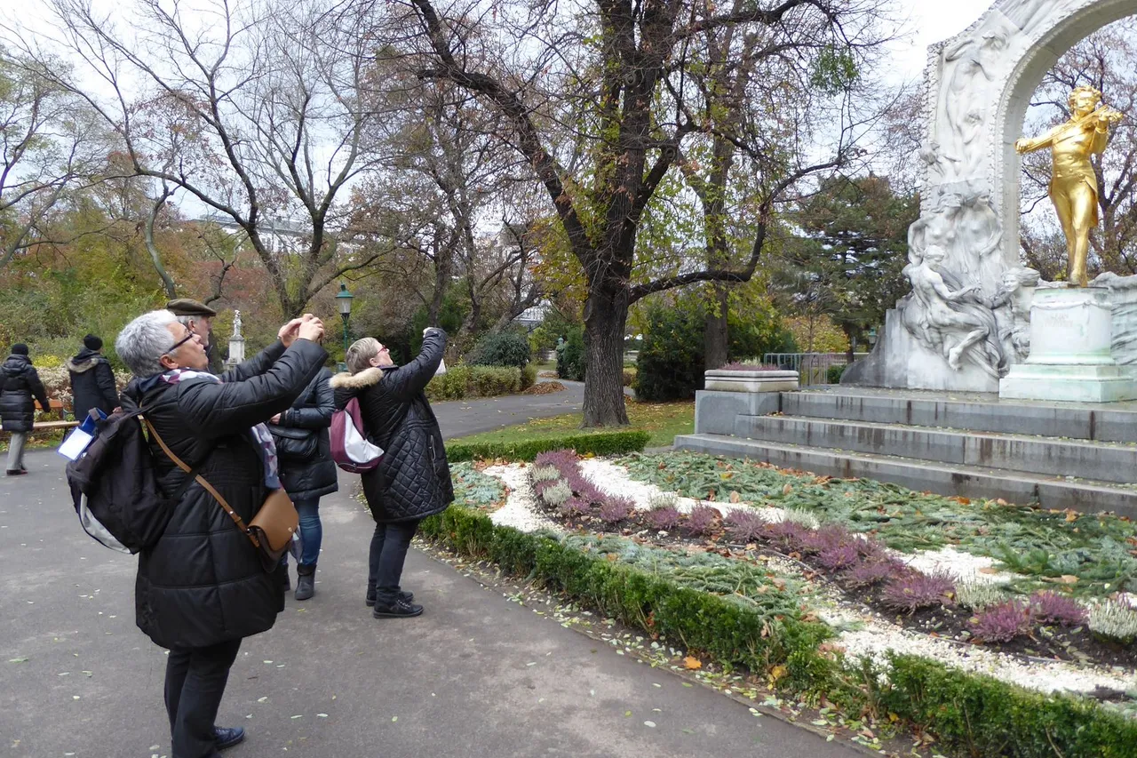 Turistai rudeniniame Vienos parke fotografuoja telefonais auksinį Johanno Strausso paminklą