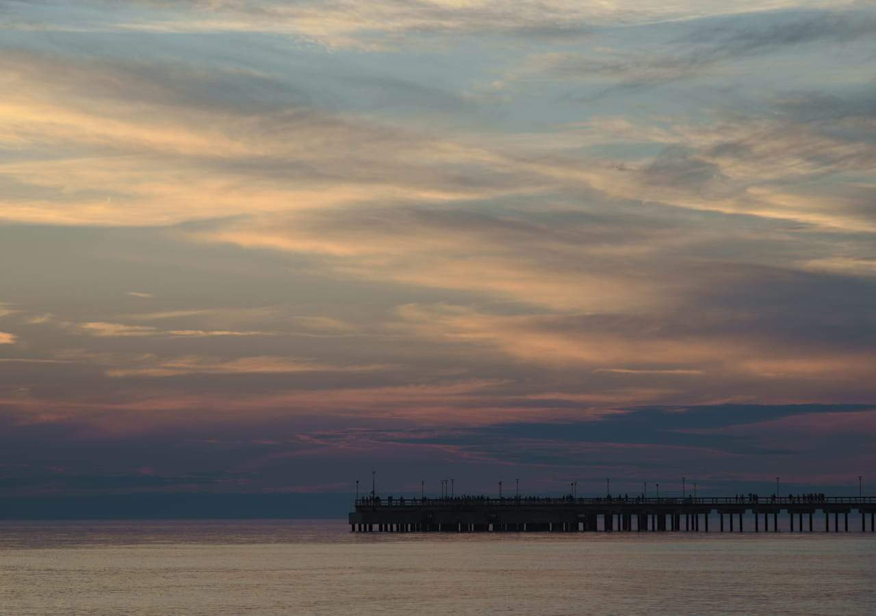 Saulėlydžio debesys virš ramios jūros ir Palangos tilto siluetas horizonte